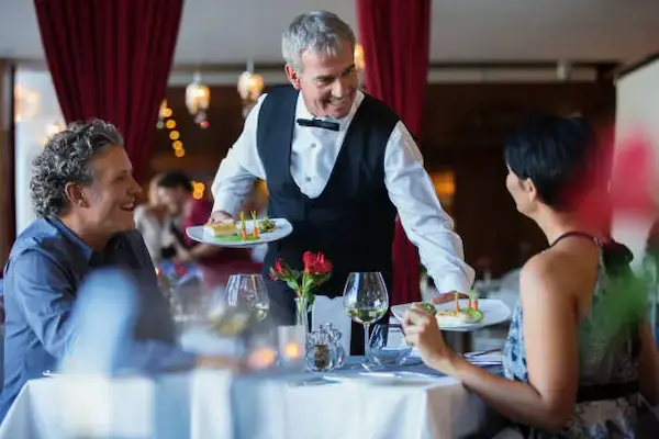 Waiter serving food to customers in restaurant